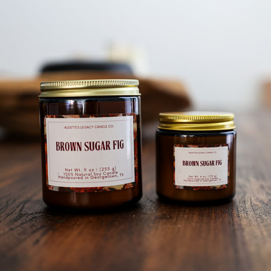 Two candles labeled 'Brown Sugar Fig' on a wooden surface with a blurred background.