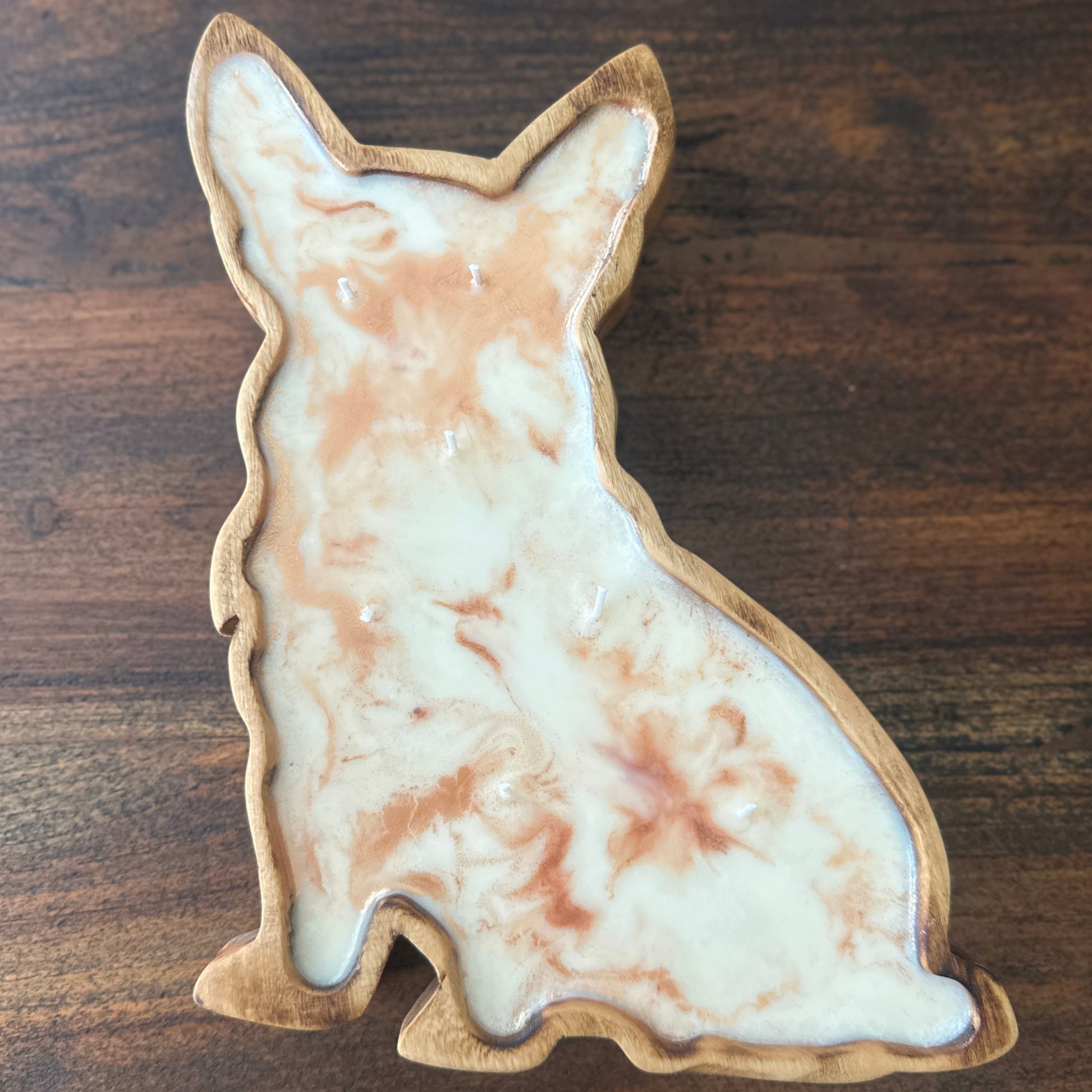 A Corgi shaped wood soy candle against a wood grain table